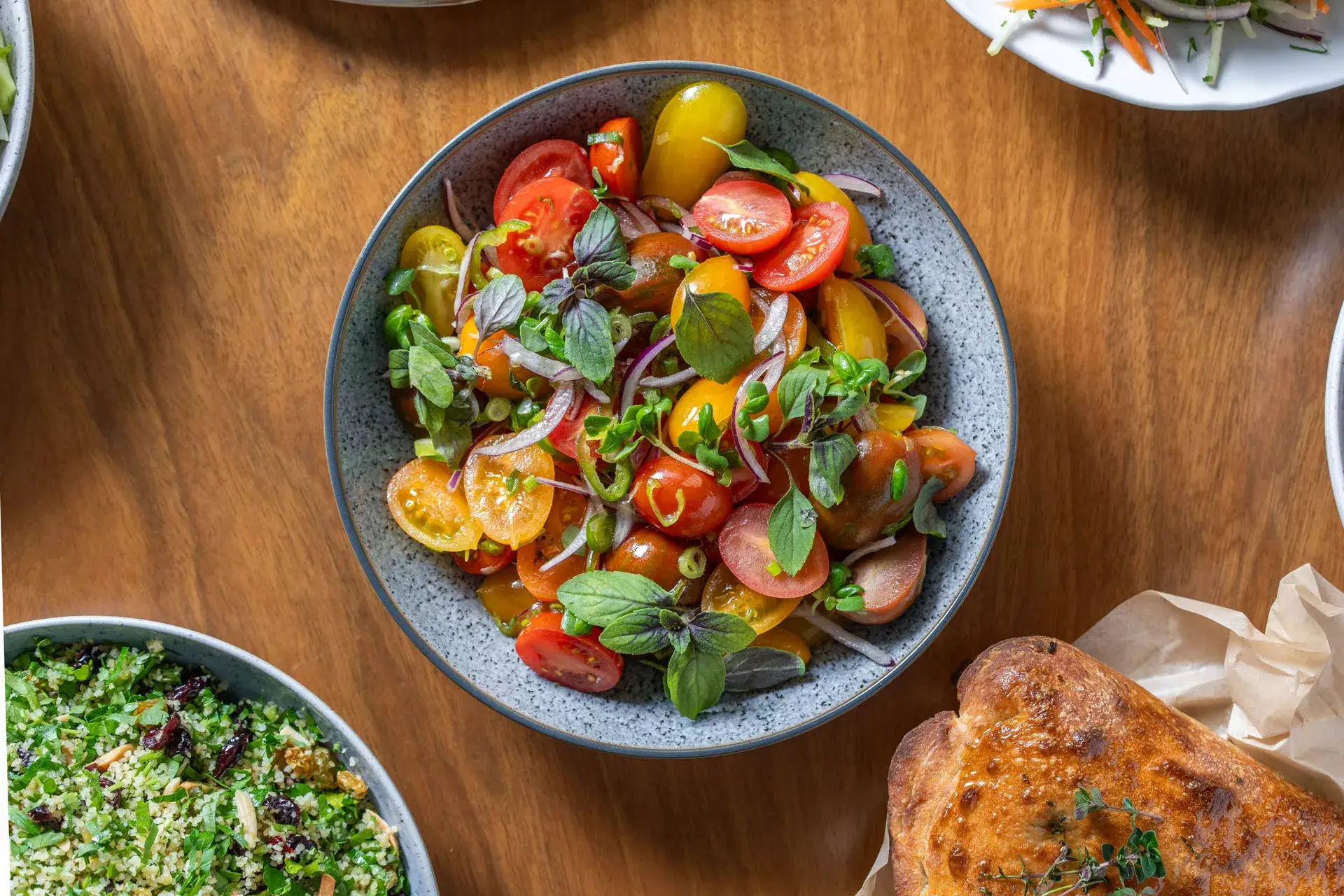 "סלט עגבניות שרי רענן בשילוב זני שרי צבעוניים, בצל סגול ועלי בזיליקום טריים – מנת פתיחה קלילה לאירועי בוטיק."