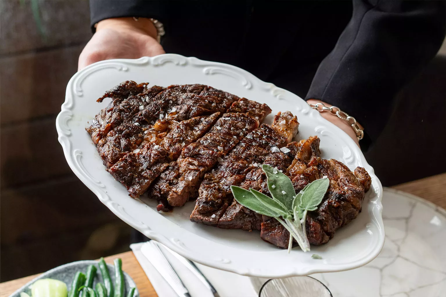 מגש סטייק בקר עסיסי בהגשה לשולחן אירוח אופי: מדגיש הגשה, שיתוף וחוויה סביב השולחן. טעימות השף