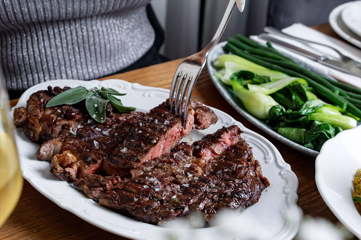 סטייק בקר פרוס מוגש על צלחת לבנה עם עשבי תיבול אופי: מדויק, נקי, מתאים לתפריט או אתר מסעדה קלאסי. טעימות השף