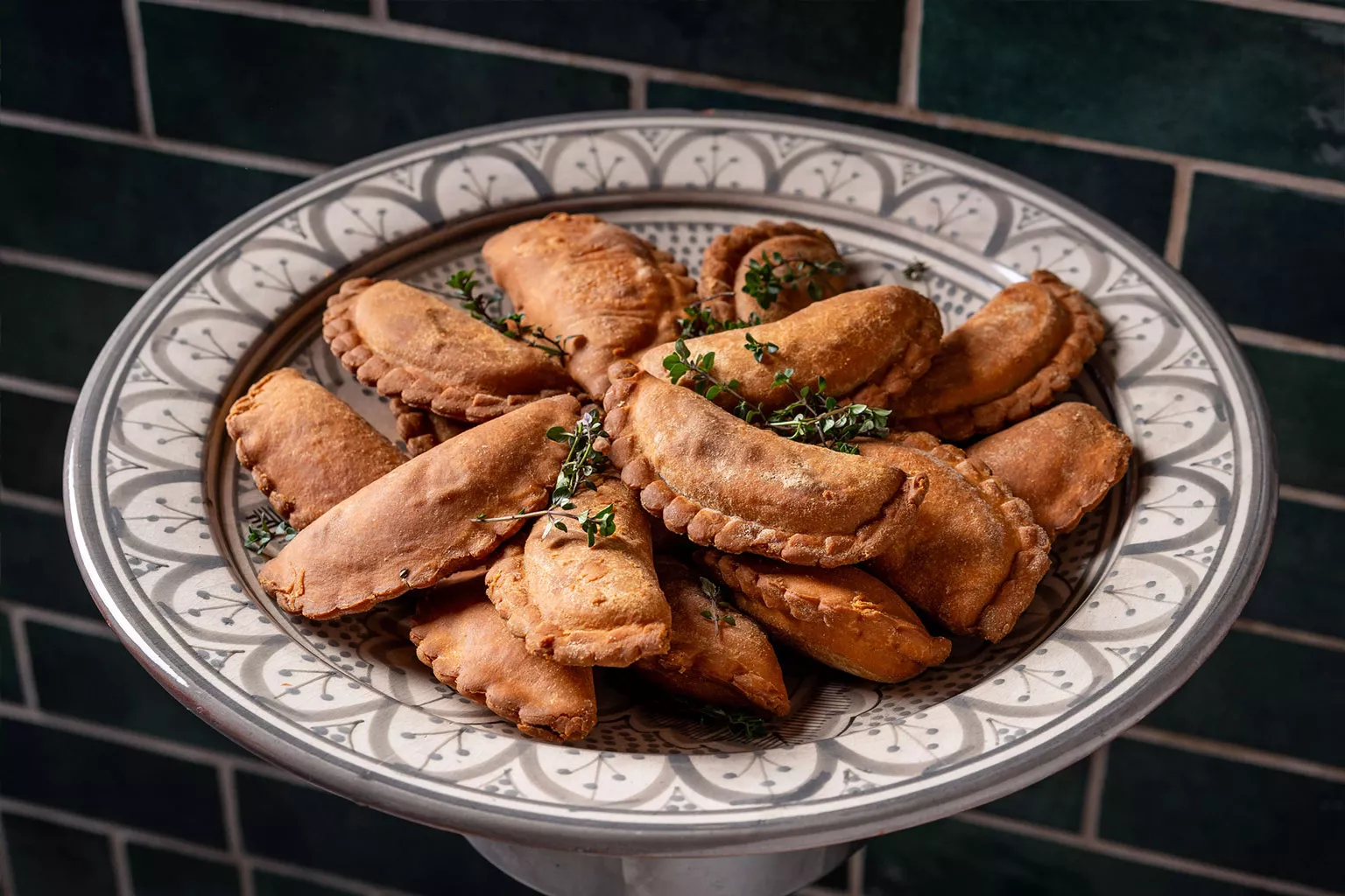 טעימות השף מאפים קטנים אפויים וממולאים מסודרים על מגש הגשה מעוטר, עם עשבי תיבול טריים מעל. צילום תקריב המדגיש מרקם זהוב והגשה מוקפדת כחלק מאירוח קולינרי.