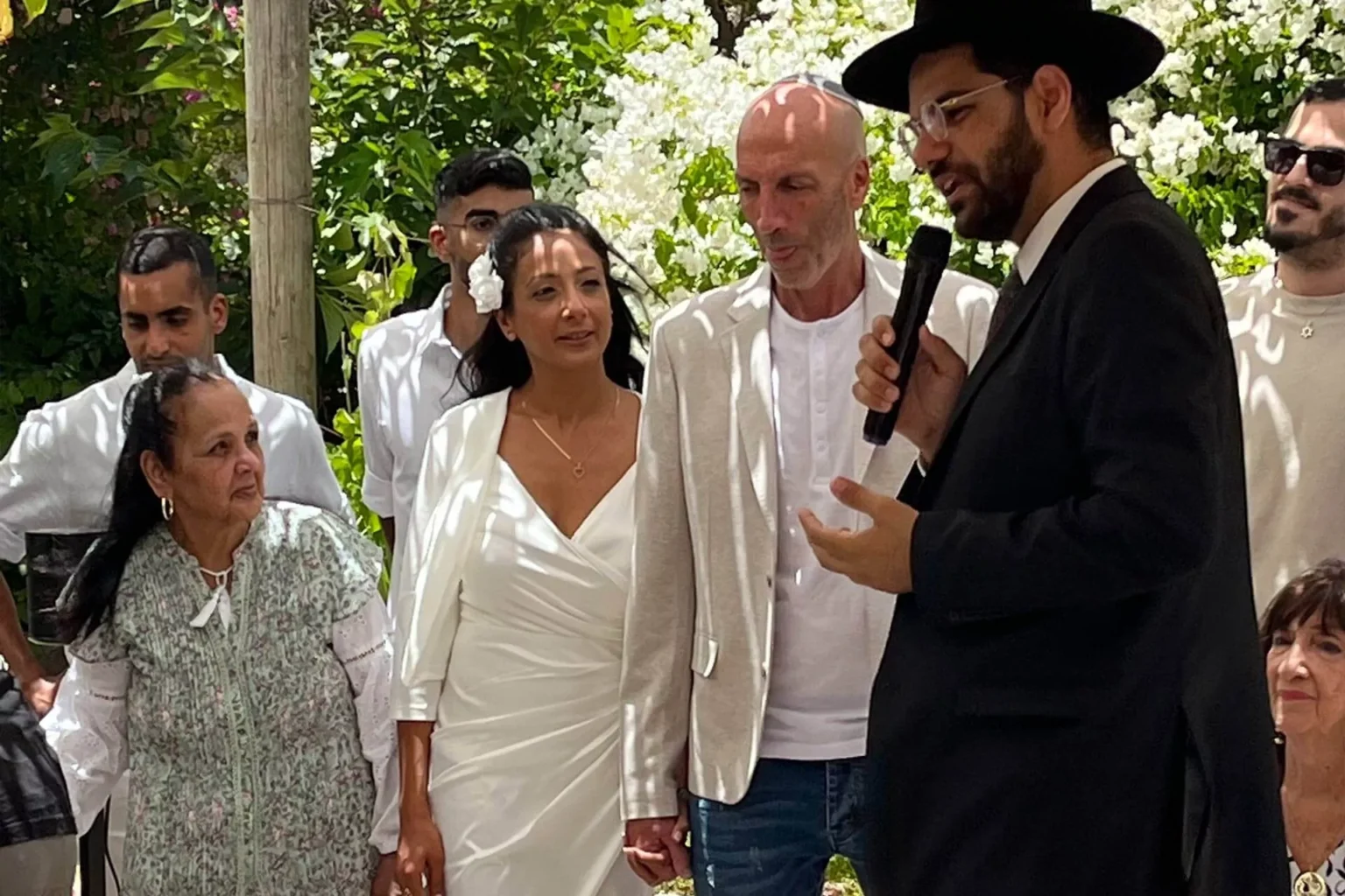 רב מדבר במיקרופון בטקס חתונה בחצר בית השף לצד הזוג ובני המשפחה